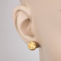 a 14k yellow gold earring with gold details on top of the earring’s surface on the earlobe of a woman with fair skin tone .This fine jewelry earring collection is designed with large earring backs for extra comfort