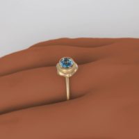 a yellow 14k gold ring worn on the finger of a woman with dark skin tone. This comfortable designer gold ring is shown with a sparkling blue topaz stone and is apart of a new fine jewelry collection on the Ezzykaia.com online boutique.