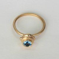 Top view of a14k yellow gold rock candy ring with bright blue topaz stone set on top of the ring. This gold minimalist ring and other fine jewelry can be seen on EzzyKaia’s online boutique and local handcrafted jewelry