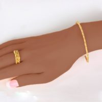 A product image presenting an 14k yellow gold bracelet on a women’s wrist with matching stackable rings on the model’s finger. Shop for this recent fine jewelry collection with excellent craftsmanship on ezzykaia.com